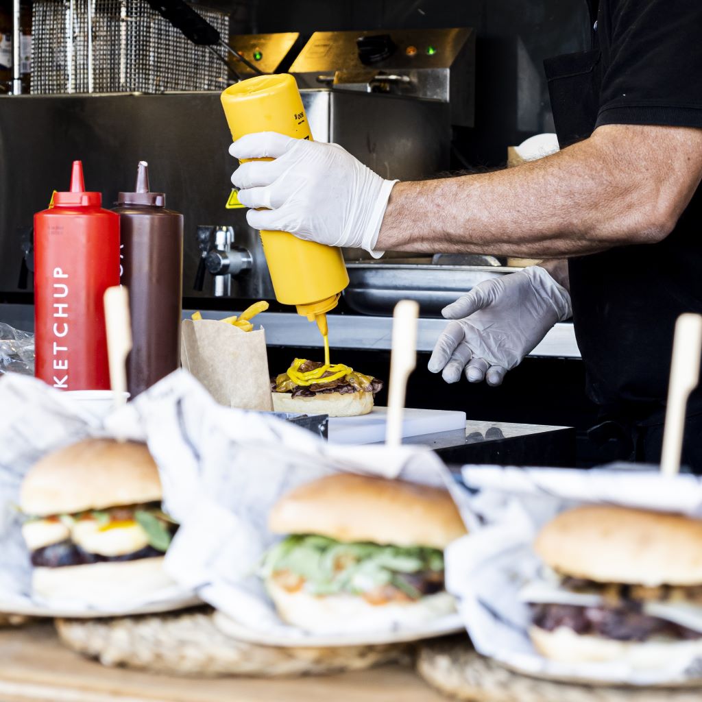 man pouring mustard on hamburger in restaurant kitchen